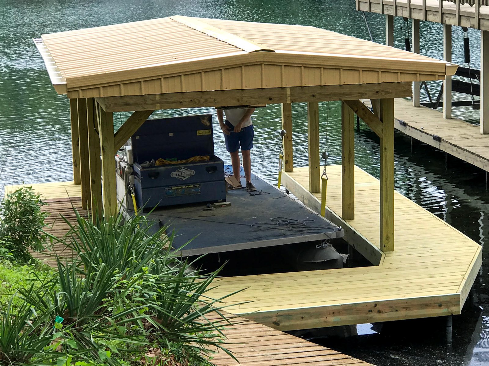Covered boat slip with timber posts, knee braces and a gable metal roof, during final build-out