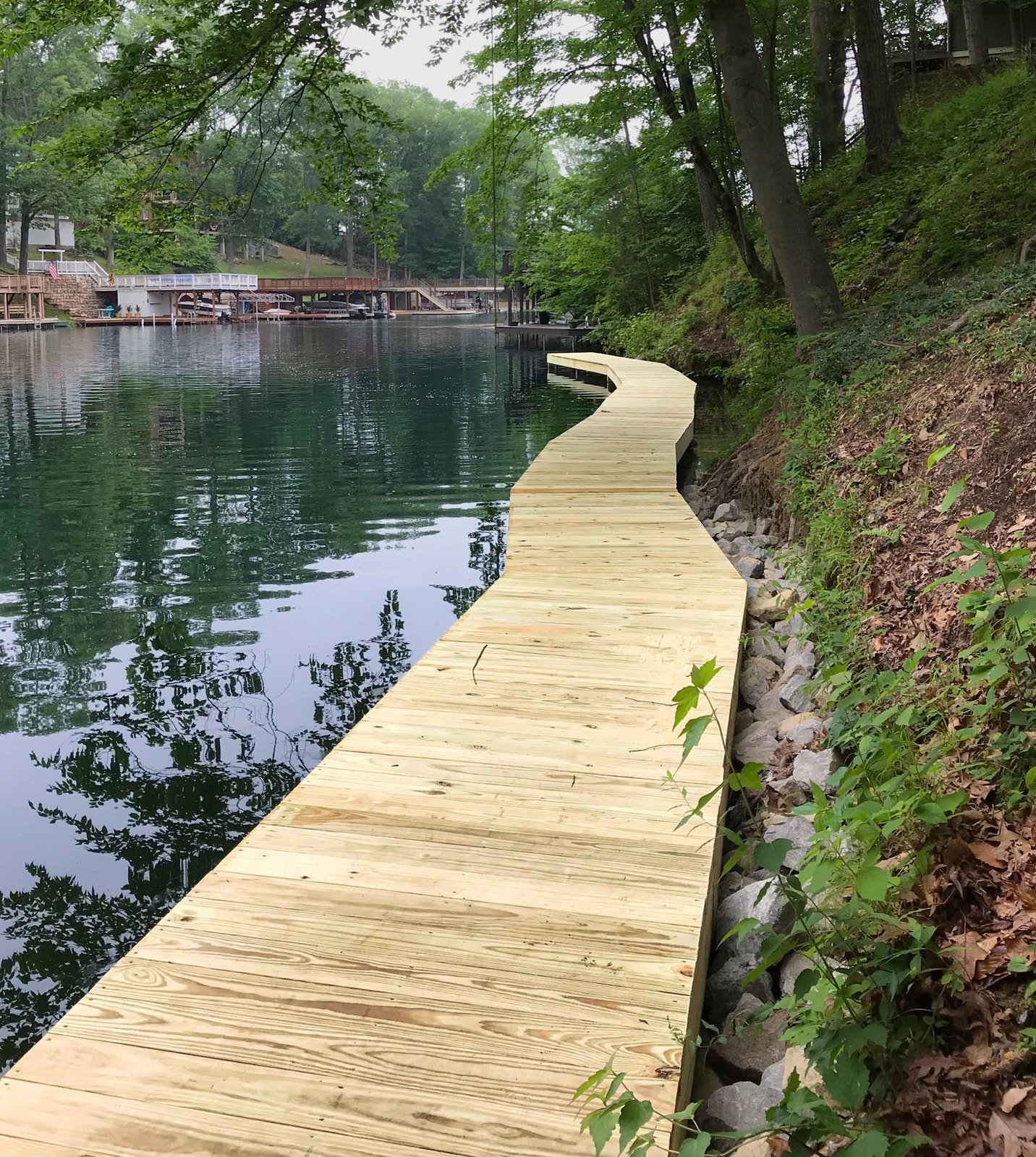 New pressure-treated boardwalk curving along a wooded lakeshore above a riprap bank